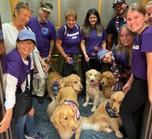Group with assistance dogs in elevator, wearing purple shirts.