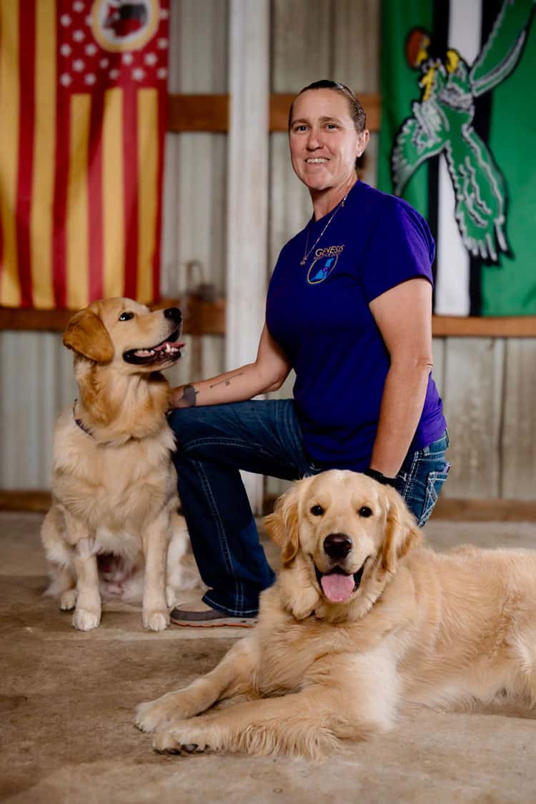 Person with two Golden Retrievers indoors, flags behind.