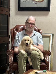 Man sitting with golden retriever puppy on chair.