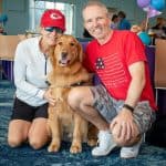 Couple smiling with golden retriever indoors.