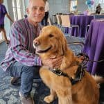 Man kneeling with a service dog indoors.