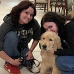 Two women with a golden retriever puppy indoors.