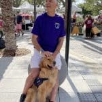 Man with service dog at outdoor market.