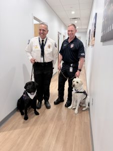 Two firefighters with service dogs in hallway.